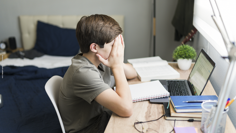 Adolescent débordé devant ses devoirs, illustrant les difficultés d’organisation scolaire et la gestion du travail à la maison.