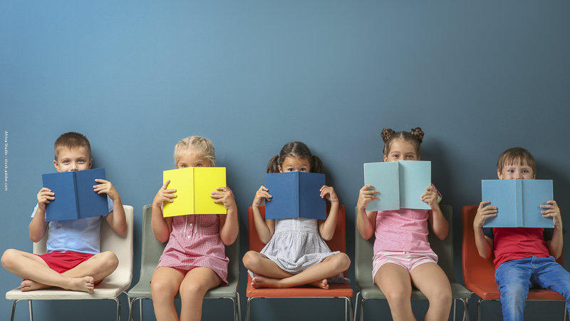Groupe d’enfants assis avec des livres devant le visage, illustrant la lecture jeunesse et le rapport des enfants aux livres.