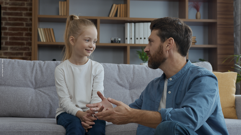 Père discutant calmement avec sa fille sur un canapé, illustrant le dialogue parent-enfant autour des émotions et des sujets difficiles.