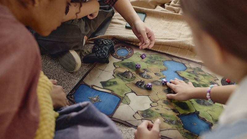 Enfants jouant à un jeu de société de plateau avec dés sur le sol, en famille loin des écrans