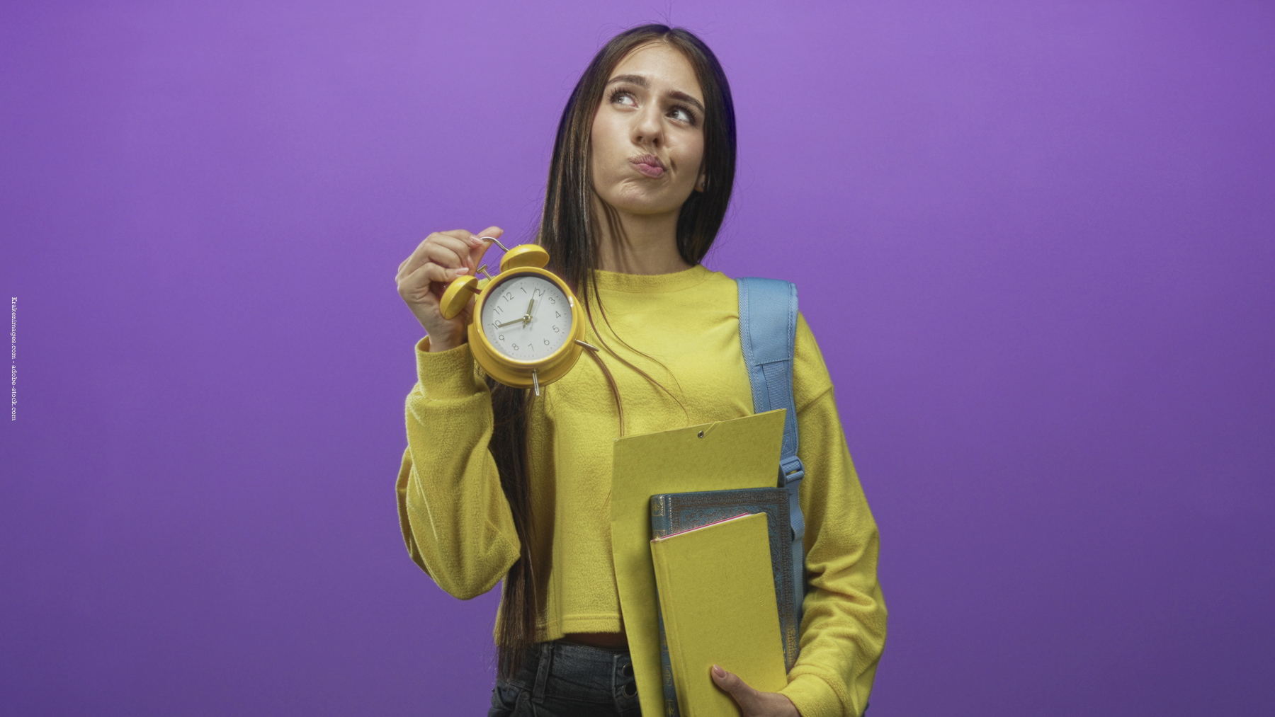 Adolescente en pull jaune tenant un réveil et des cahiers sur fond violet, l’air pensif