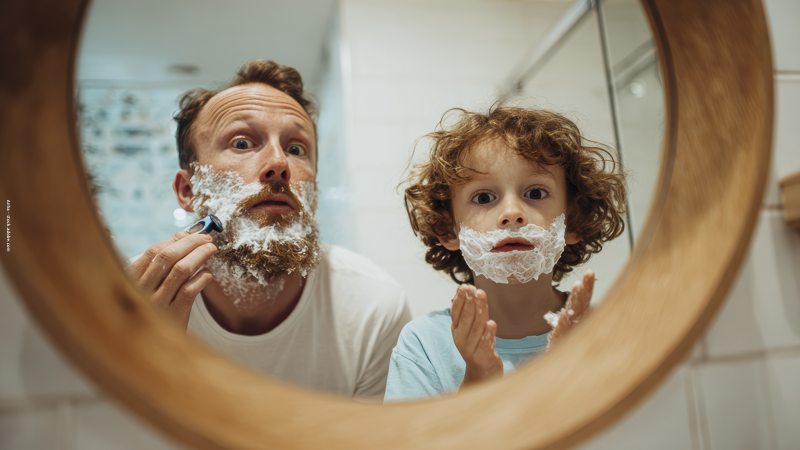 Père et enfant devant un miroir, se rasant avec de la mousse, illustrant l’imitation des modèles parentaux et le développement de l’identité.