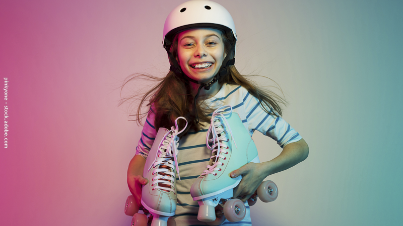 Enfant souriant portant un casque et tenant des rollers, prêt à apprendre à faire du roller en toute sécurité.