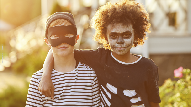 Deux enfants déguisés pour Halloween en squelette et en super-héros, souriants et complices, prêts pour la chasse aux bonbons en automne.