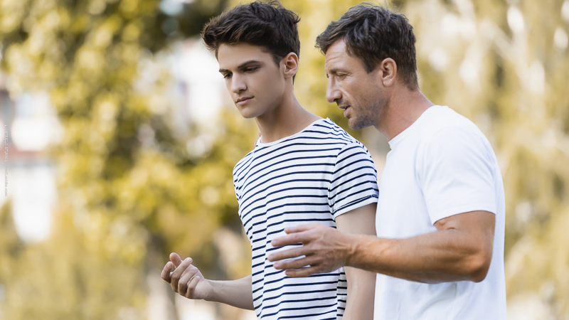 Adolescent marchant avec son père dans un parc, symbole de communication bienveillante et de relation parent-ado.