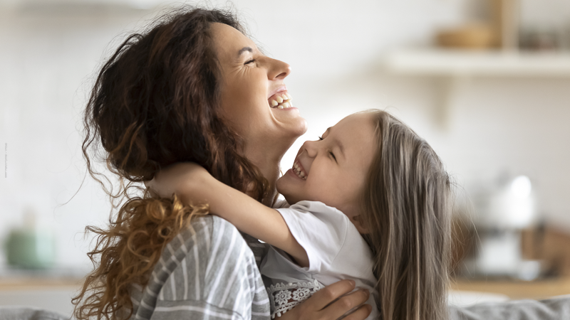 Une mère rit aux éclats avec sa fille dans ses bras, illustrant la complicité et la force des mamans solos face aux défis du quotidien.