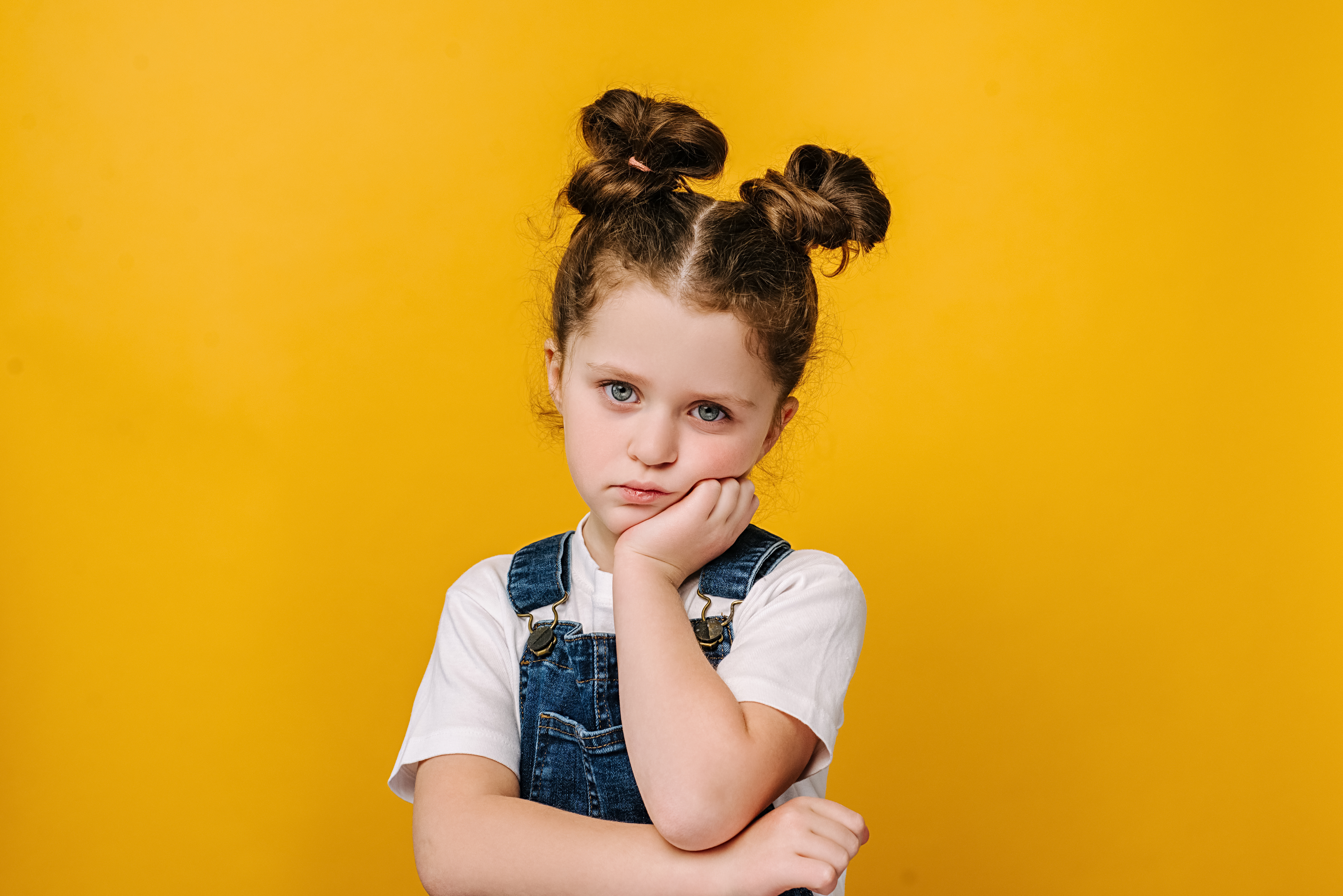 Petite fille l'air boudeur, menton dans la main et bras croisés sur fond jaune — enfant qui abandonne face aux difficultés