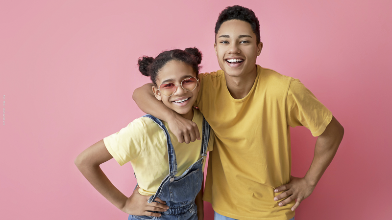 Frère et sœur souriants posant ensemble, complices malgré leurs différences : symbole de la fraternité et des relations à apaiser pendant les vacances.