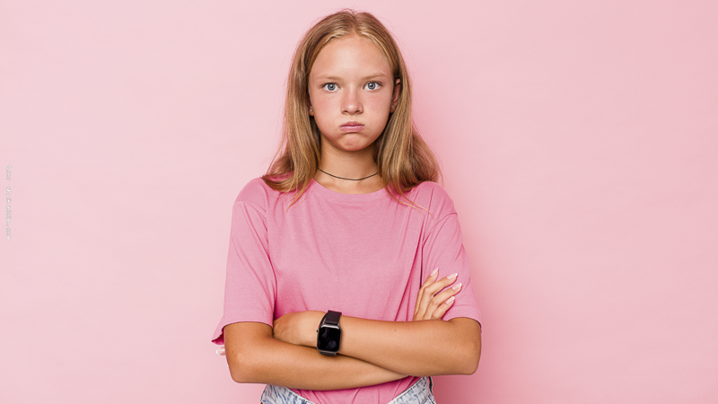 Enfant bras croisés avec expression fermée, illustrant un refus d’obéir et des difficultés à respecter les règles familiales.