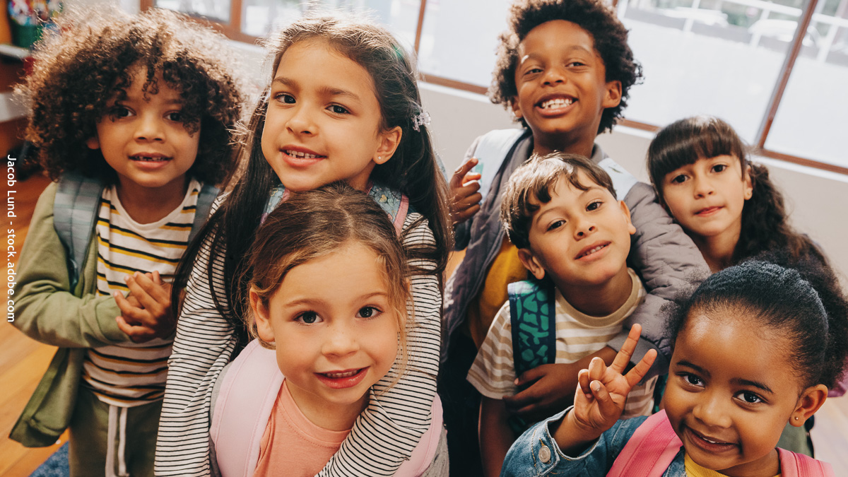 Groupe d’enfants souriants de différentes origines à l’école, symbole de mixité sociale et culturelle dès la rentrée.