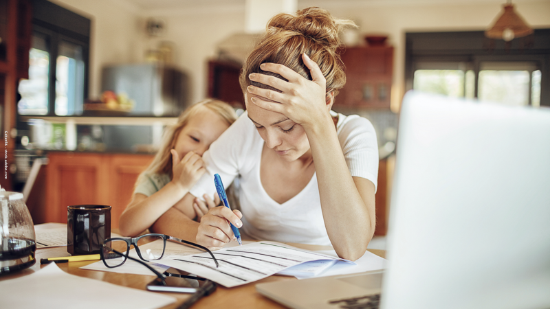 Une mère célibataire concentrée sur ses papiers administratifs pendant que son enfant l’enlace, illustrant les démarches du RSA majoré pour parents isolés.