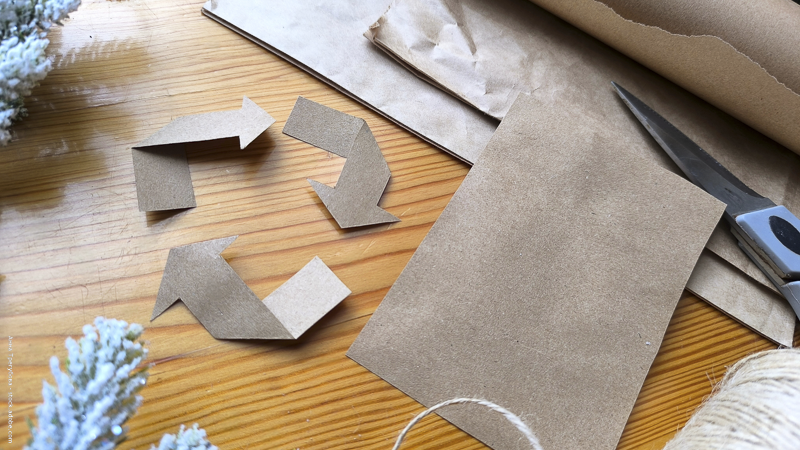 Matériel d’emballage recyclé posé sur une table en bois, avec symbole de recyclage en carton — illustration des cadeaux de seconde main et du zéro déchet.