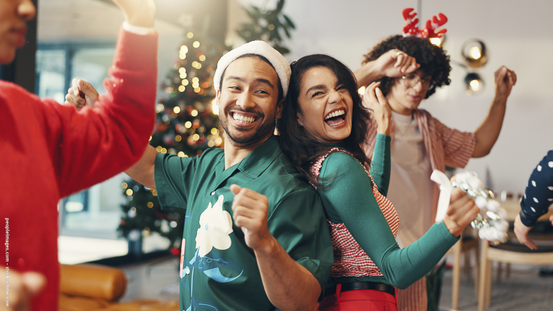 Groupe d’amis qui dansent et s’amusent devant un sapin de Noël — ambiance festive et conviviale lors d’un Noël entre amis.