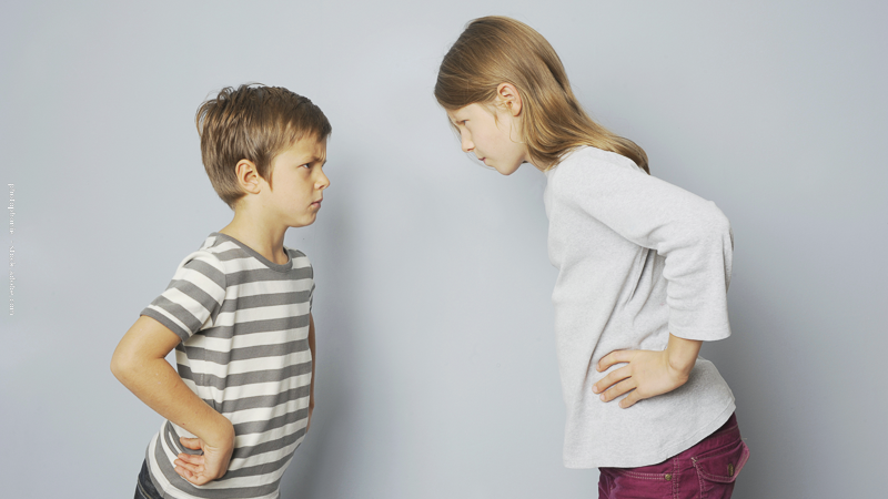 Deux enfants se font face en se regardant avec sérieux, mains sur les hanches, illustrant une dispute entre frère et sœur.