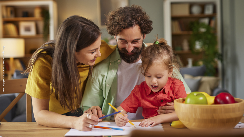 Parent et enfant dessinent ensemble autour d’une table, partageant un moment créatif et complice lors d’une activité artistique en famille.
