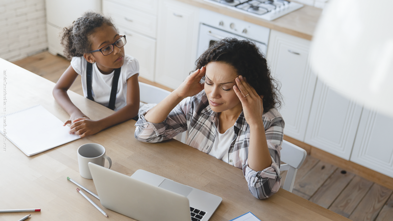 Mère fatiguée devant un ordinateur pendant que son enfant la regarde, illustrant la charge mentale et la solitude parentale.Mère fatiguée devant un ordinateur pendant que son enfant la regarde, illustrant la charge mentale et la solitude parentale.