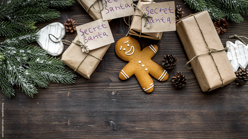Cadeaux emballés façon Secret Santa posés sur une table en bois avec décorations naturelles et biscuit bonhomme en pain d’épices — ambiance Noël conviviale.